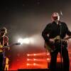 Two guitarists perform on a stage that is bathed in red light