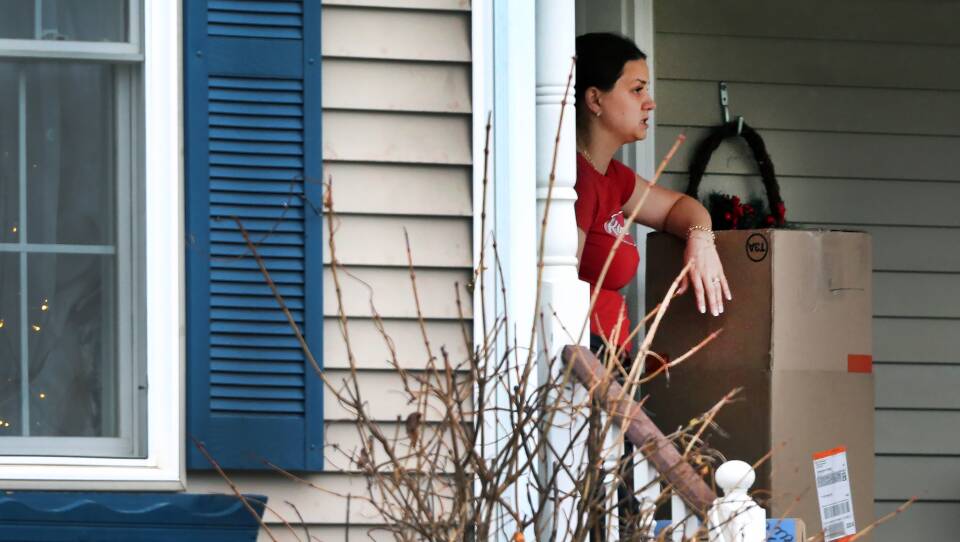 A woman stands on a porch with her arm resting on a cardboard box.