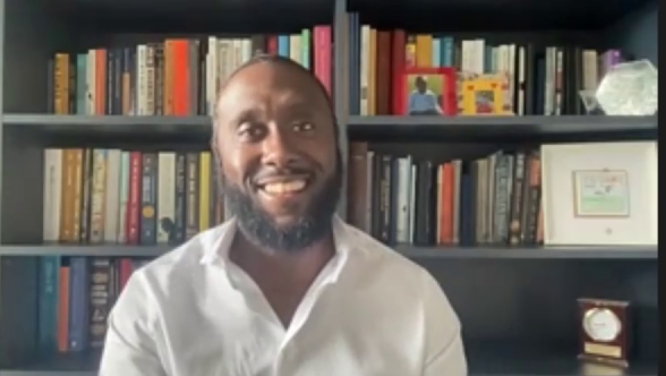 A man sitting, smiling, in front of a bookshelf.