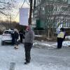 Five people, some holding anti-vaccine mandate signs and others with bullhorns, stand on a street with small snowbanks behind them.