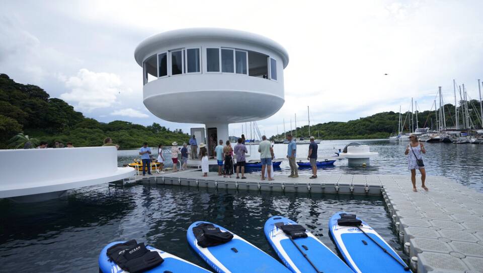People standing on a dock looking up at a round "house" on top of a pillar.