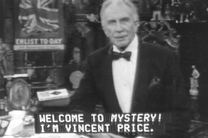 On a grainy, black and white television screen, an elderly man in a tuxedo sits in an ornate high-backed chair at a desk and addresses the camera.