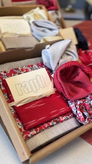 Sustainable wrapping paper, which is red, patterned and grey, sits in a box ready to gift.