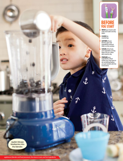A boy wearing a blue shirt is pouring a cup of blueberries into a blender to make a smoothie.