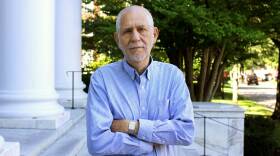 A man with his arms crossed stands on the marble stairs of a university campus.