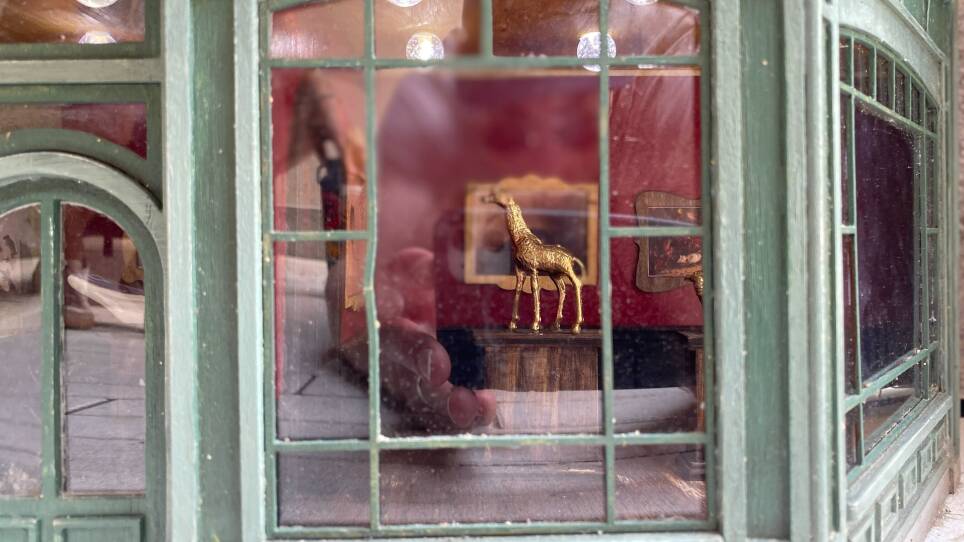 A small sculpture of a golden giraffe, seen through a small window with a green frame.