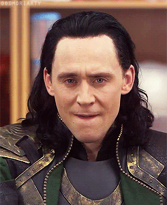 Tom Hiddleston as Loki — A pale man with shoulder length black hair in a burnished gold and green tunic — rolls his eyes and sighs.