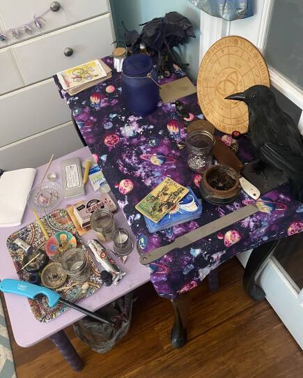 A small table strewn with tarot cards, candles, and a stuffed crow.