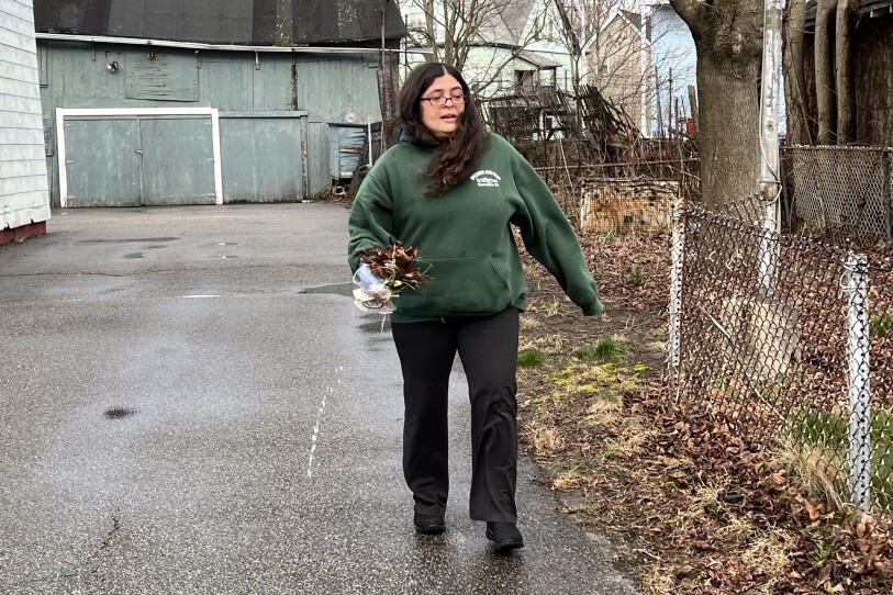 A woman in a green sweatshirt holds a plastic cup and other small trash in one hand.