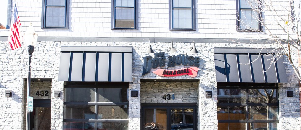 The outside of a Woburn restaurant called The Dog House Bar and Grill with an American Flag hanging to left of it.