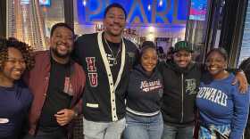 Six people stand, arms wrapped around one another, and smile at a party.