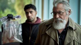 Eddie Suleman (Azan Ahmed) holds an evidence bag while Hendrik Davie (Darrell D'Silva) sulks.