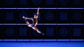 John Lam performs in Stephen Galloway's DEVIL'S/eye as part of Boston Ballet's "My Obsession." The dancer is photographed mid-air above a blue stage, with a dark blue and black background behind him