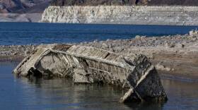A boat wreck, covered with barnacles, lying sideways in the water of a lake