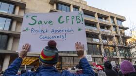 A person holds up a sign in a protest that reads "Save CFPB: Protect American consumers"