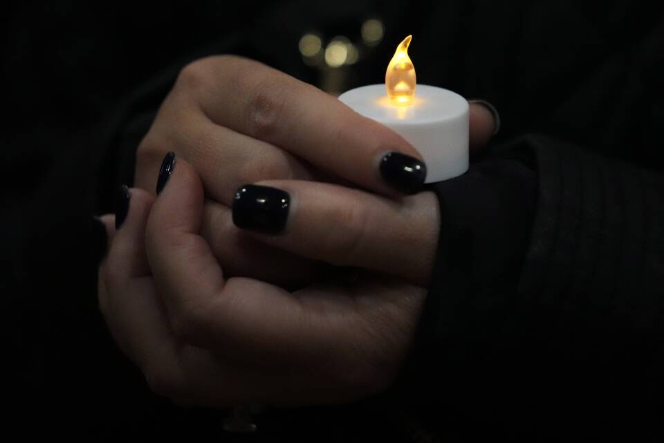 A close-up of a hand with black nail polish holding a small battery-operated candle.