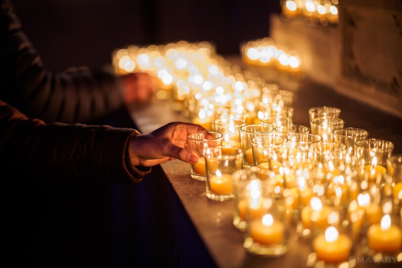 A hand holds a small votive candle among many other identical candles at Mount Auburn Cemetery