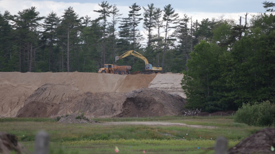 An excavator works amid piles of sand.