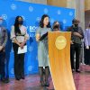 The mayor stands at a podium in front of a group of seven, all wearing masks (pictured mid-speech).